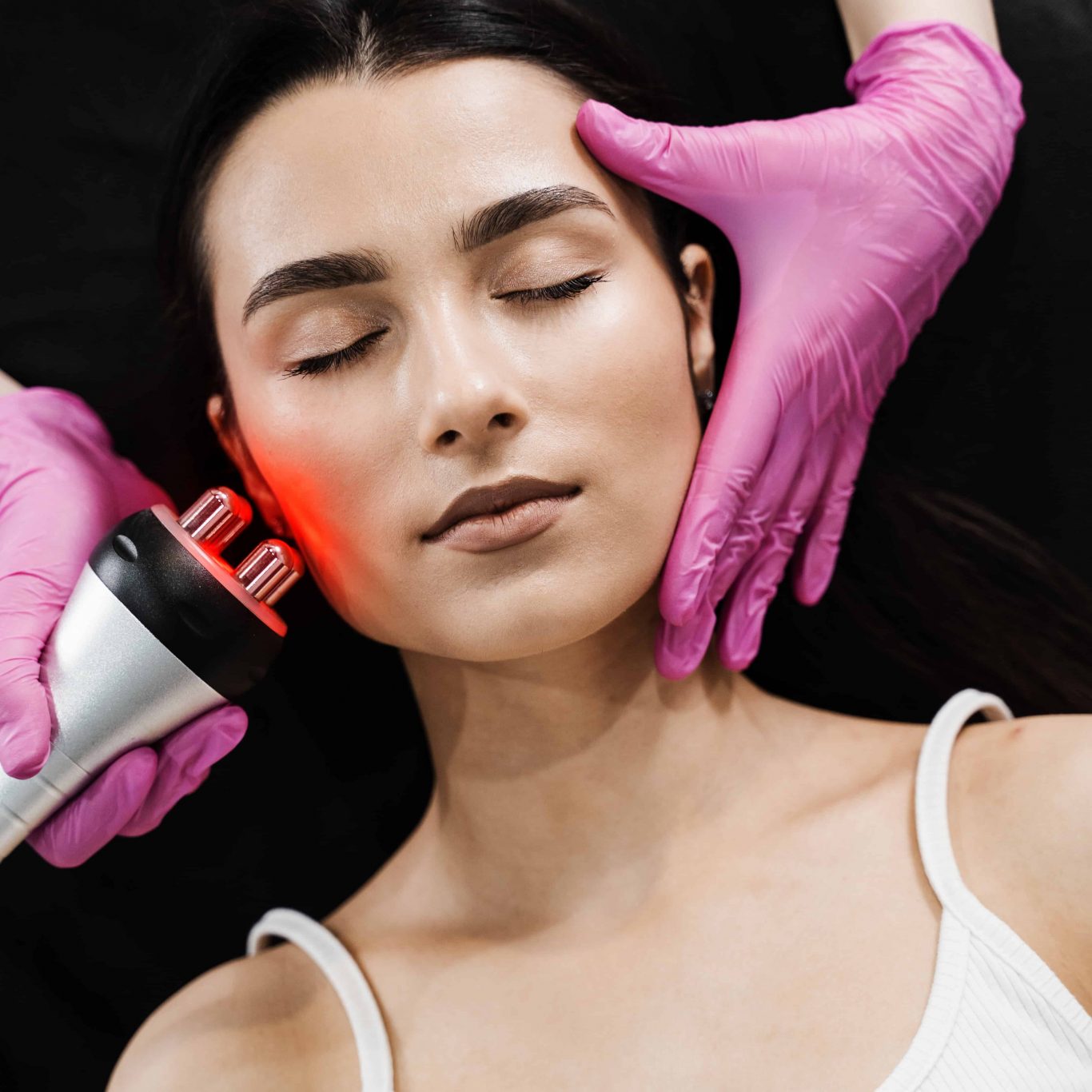 Professionelle Radiofrequenz-Gesichtsbehandlung im Kosmetikstudio zur Hautstraffung und Faltenreduktion. Ein Handstück mit rotem Licht wird über die Wange einer entspannten Kundin geführt.