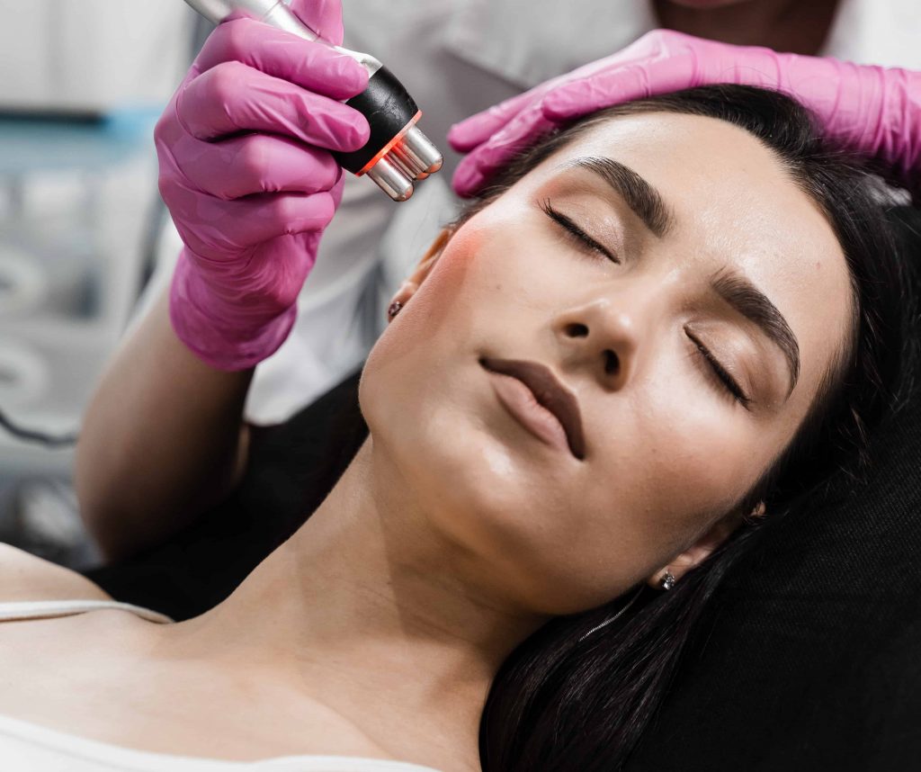 Professionelle Radiofrequenz-Gesichtsbehandlung im Kosmetikstudio zur Hautstraffung und Faltenreduktion. Ein Handstück mit rotem Licht wird über die Wange einer entspannten Kundin geführt.